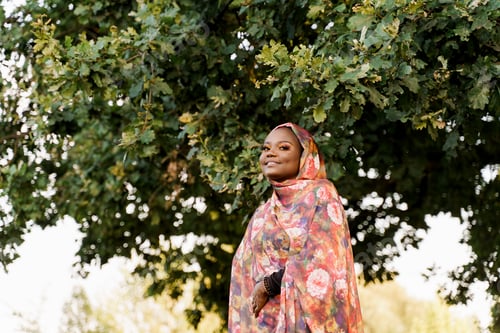 Preview: Black Muslim woman in colorful hijab smiling under tree, African fashion and lifestyle