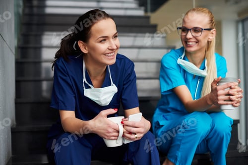 Vista previa: Two surgeons taking a break, sitting on steps, holding coffee cups, smiling