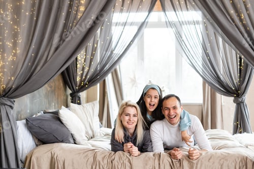 Preview: Top view of beautiful young mother, father and their daughter smiling while lying on bed