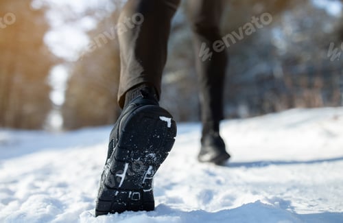 Preview: Outdoor winter activities. Male athlete in sports shoes jogging at park on snowy winter day, closeup