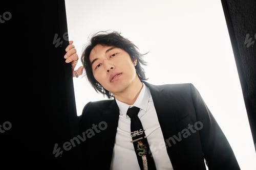 Preview: Stylish young Asian man poses confidently in modern attire against a minimalist backdrop