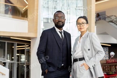 Preview: Two young elegant employees in suits standing inside large business center