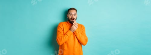 Preview: Scared and shocked guy looking at camera, standing in orange sweater against turquoise background