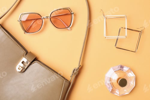 Preview: Beautiful bag, perfume and stylish accessories on pale orange background, flat lay