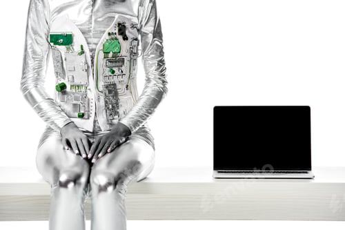 Preview: cropped image of robot sitting on table near laptop with blank screen isolated on white, future