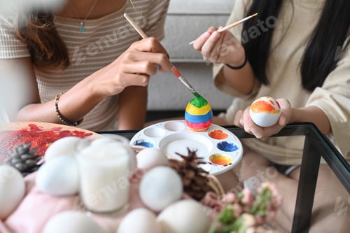 Preview: Mother helping her daughter painting easter eggs. Easter, holidays and people concept.