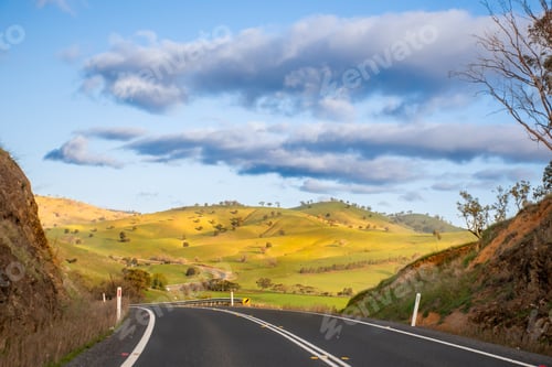 Preview: Open empty road surrounded by green hills, fields and farms in Australia. Road trip background