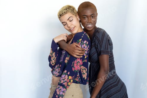 Preview: Multiethnic joyful ladies embrace and enjoy togetherness while looking at camera against background.