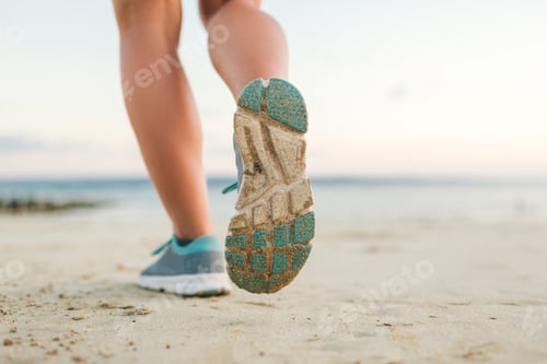 Preview: cropped shot of female jogger running on sandy beach