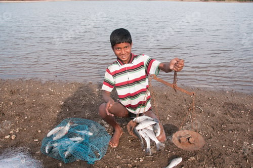 Preview: Young Fisherman take fish out of the net in front lake, India.