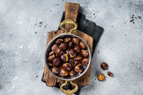 Preview: Cracked roasted chestnuts served in a skillet. Gray background. Top view