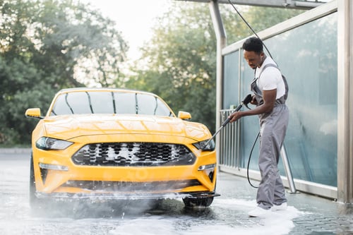 Preview: Man washing his luxury yellow car under high pressure water jet