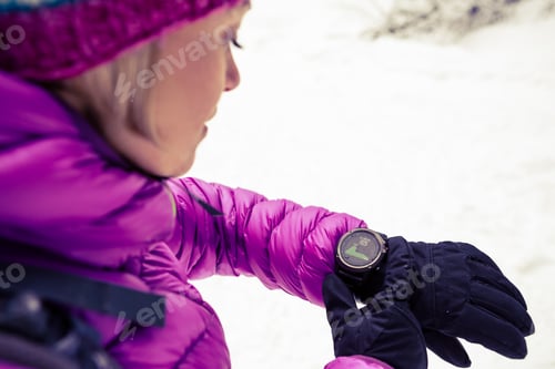 Preview: Woman hiker checking sports watch in winter woods and mountains