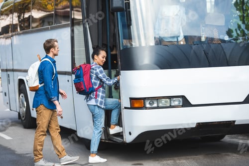 Preview: multiethnic couple of tourists with backpacks walking into travel bus at street