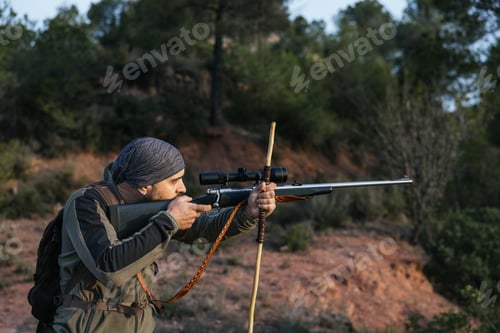 Preview: Hunter aiming with rifle in forest at sunset