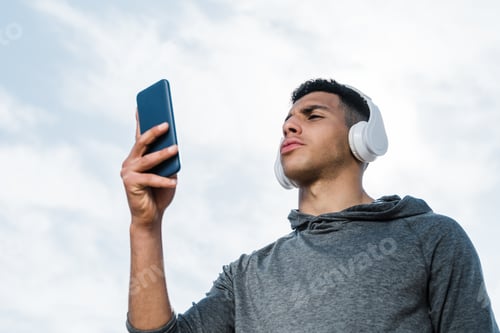 Preview: Young Man Listening with Headphones Holding Smart Phone