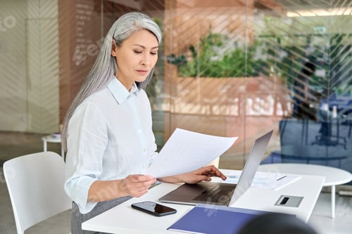 Preview: Serious mid age businesswoman doing paperwork using pc laptop computer.