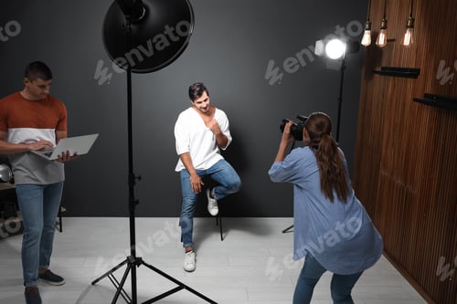 Preview: Professional photographer with assistant taking picture of young man in modern studio