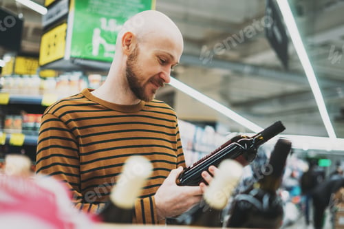 Preview: Adult bald bearded man chooses wine at supermarket