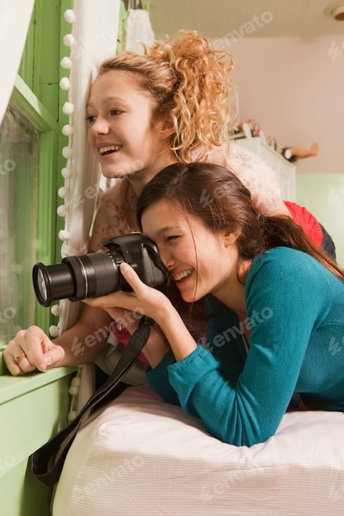 Preview: Teenage girls looking through window taking photograph