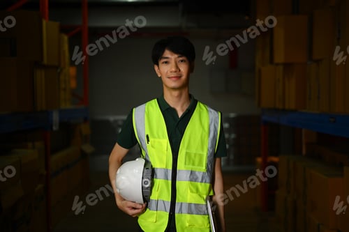 Preview: Image of handsome male warehouse worker standing aisle between rows of tall shelves.