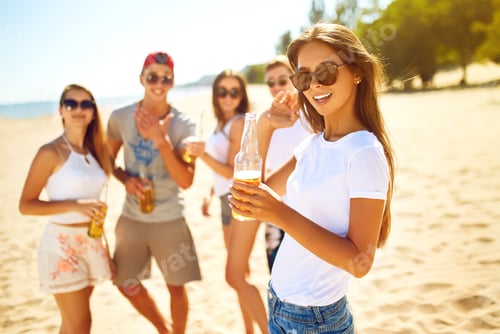 Preview: Smiling young girl with beer. other while people barbecuing in the background. Fun at the beach.
