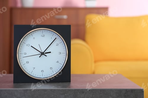 Preview: Stylish clock on table against blurred background. Time of day