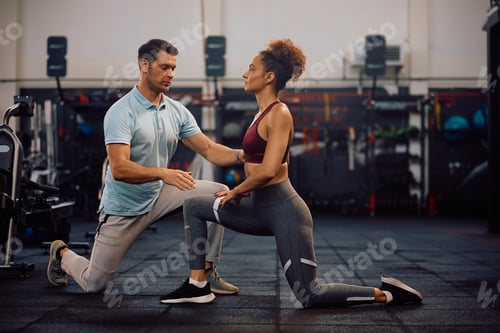 Preview: Young sportswoman doing stretching exercises while working out with a coach in health club.