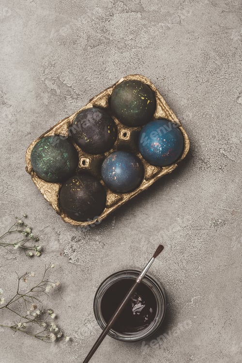 Preview: top view of painted easter eggs in golden tray with paint and brush on concrete