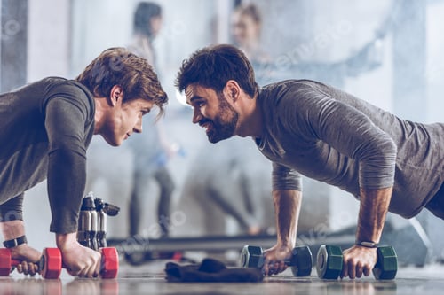Preview: athletic young sportsmen doing push ups with dumbbells at the gym, gym workout concept