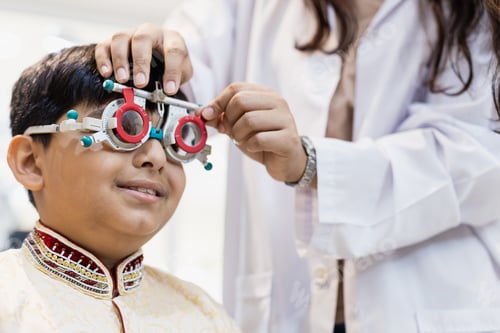 Preview: Happy Indian child boy examining eyesight modern ophthalmology equipment in clinic.