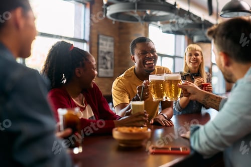 Preview: Cheerful black man toasting with his friends while drinking beer in a pub.