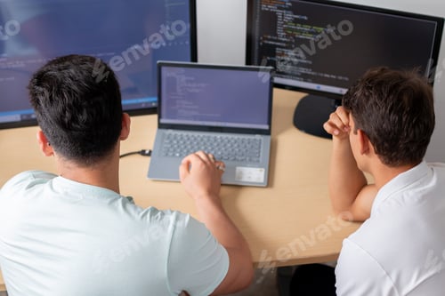 Preview: Two young programmers in an office, preoccupied as they work on a programming and technology project