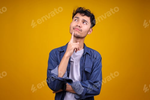 Preview: Young Asian Man Having Doubts While Looking Up Over Isolated Yellow Background