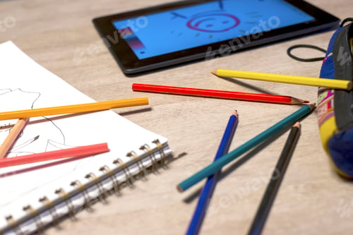 Preview: Above view of open exercise book, pencil crayons and tablet on white desk