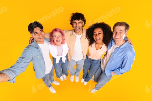 Preview: Happy international group of teenager friends embracing and taking selfie over yellow studio