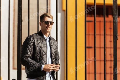 Preview: Man in jacket stands near fence in sunlight