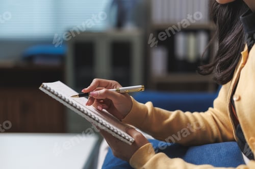 Preview: Businesswoman writing notes in notebook at office