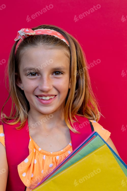 Preview: Happy caucasian schoolgirl with school bag and books over pink background at elementary school