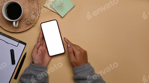Preview: Female hands holding smart phone with white screen on beige background.