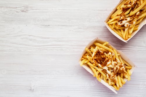 Preview: French fries with cheese sauce and fried onion in paper boxes on a white wooden table