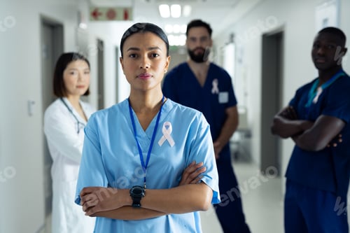 Preview: Portrait of biracial female healthcare worker with cancer ribbon in busy hospital corridor