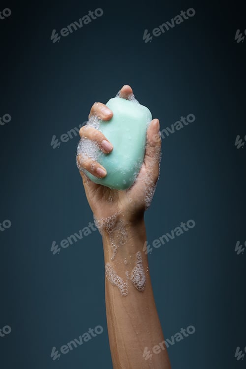 Preview: Hand holding a bar of green soap on a dark blue background - beating coronavirus concept