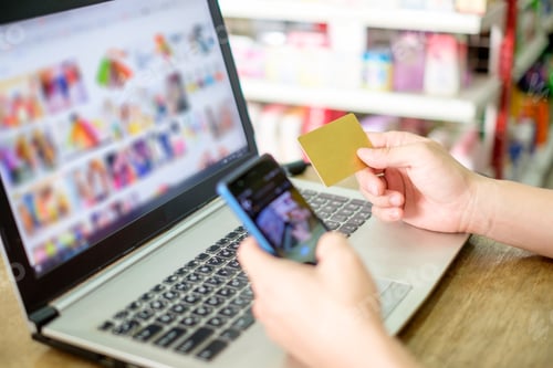 Preview: Hand holding credit card and using laptop with smartphone for payment shopping online