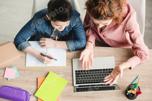 Preview: top view of mother and son sitting at desk with laptop and notebooks and doing homework together