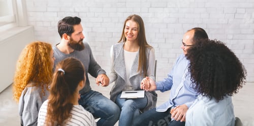 Preview: Diverse people sitting on chairs in circle holding hands