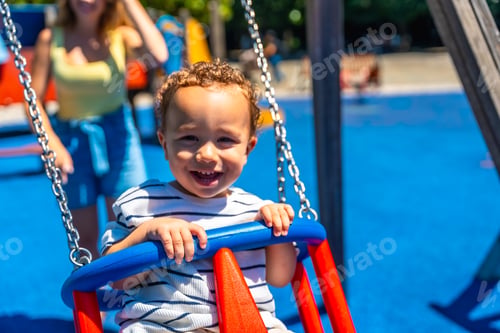Preview: Happy toddler smiling and having fun on a swing at the playground