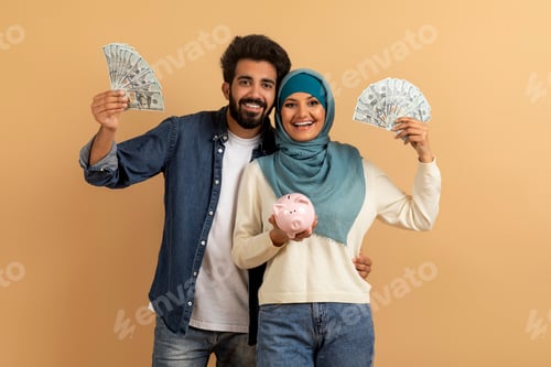 Preview: Money Saving. Happy Muslim Couple Holding Piggybank And Dollar Cash In Hands
