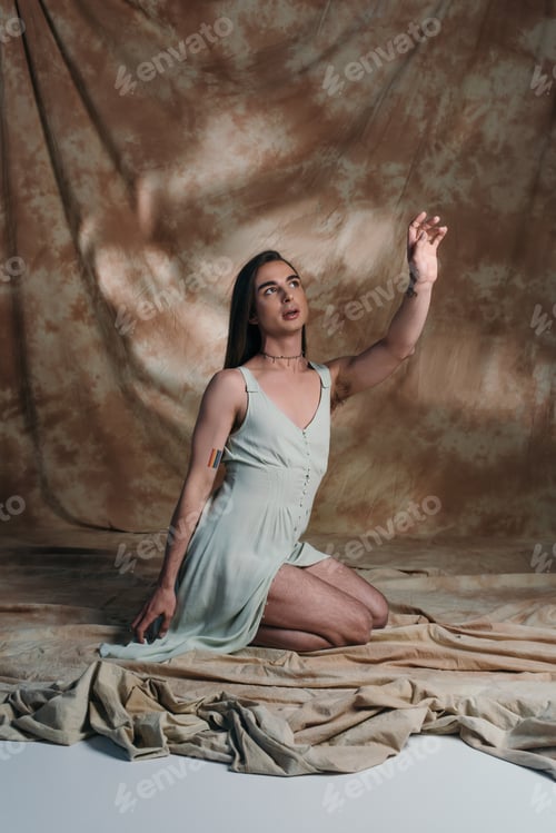 Preview: Nonbinary person in sundress sitting and gesturing on abstract brown background