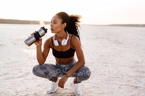 Preview: Image of african american sportswoman drinking water while squatting